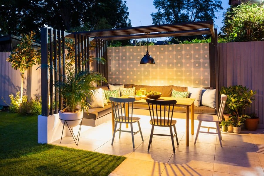 Stylish outdoor dining area with a modern pergola, cozy seating, vibrant cushions, potted plants, and warm evening lighting