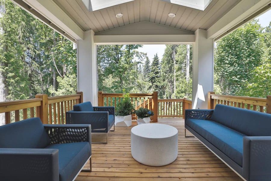 Cozy covered porch with modern blue seating, a minimalist round table, and views of lush greenery