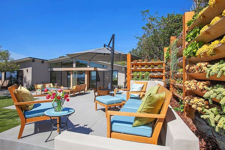 Vibrant patio with wooden furniture, colorful cushions, a vertical succulent garden, and a modern home backdrop under a clear blue sky