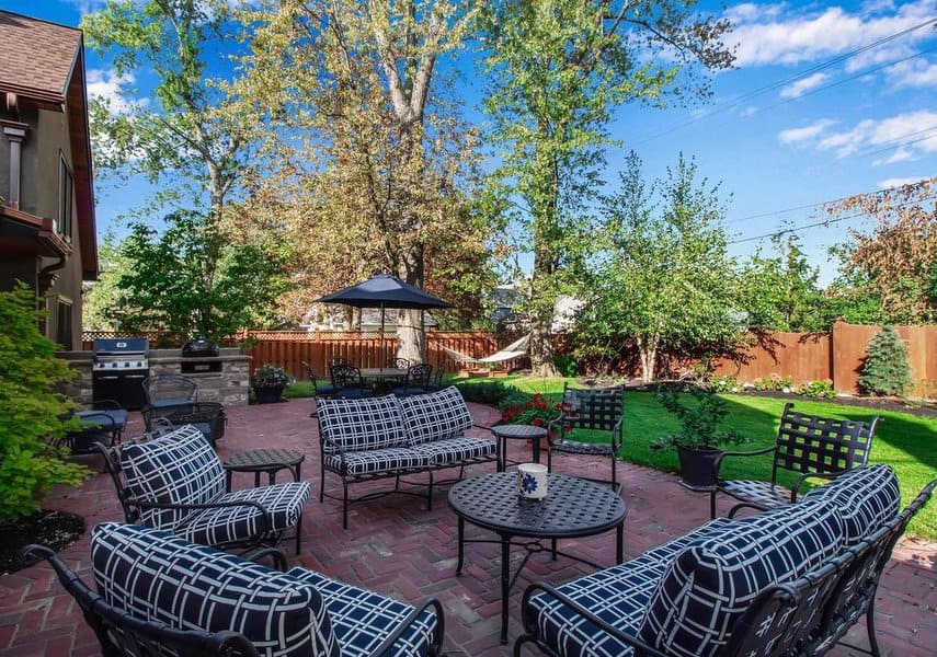 Charming backyard patio with patterned black-and-white seating, a brick floor, umbrella shade, and a lush garden setting