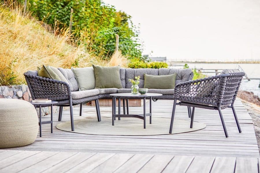 Cozy outdoor seating on a wooden deck with woven chairs, green cushions, and a serene waterfront backdrop