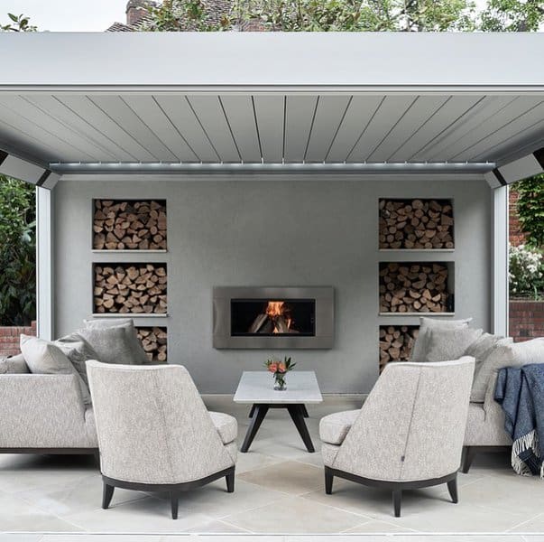 Modern outdoor lounge with gray armchairs, a sleek fireplace, and stacked firewood accents in a covered patio setting