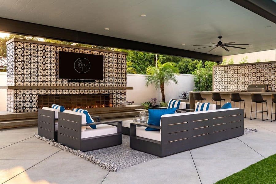 Modern outdoor lounge with patterned fireplace, built-in TV, sleek seating, bar area, and tropical landscaping for a stylish retreat