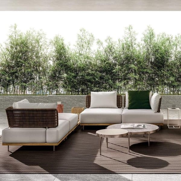 Modern outdoor lounge with woven rattan furniture, plush white cushions, and lush bamboo greenery in the background