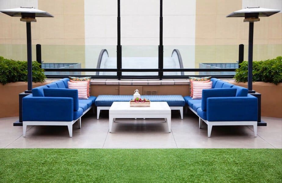 Vibrant rooftop patio with bold blue seating, white coffee table, and lush greenery, perfect for modern outdoor relaxation