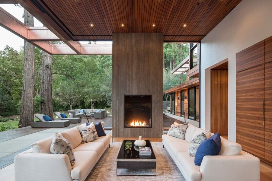 Luxurious outdoor living area featuring a modern fireplace, plush sofas, and a seamless connection to lush natural surroundings