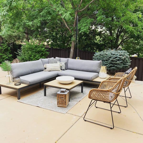 Outdoor patio with gray sectional sofa, wicker chairs, and a table under green trees