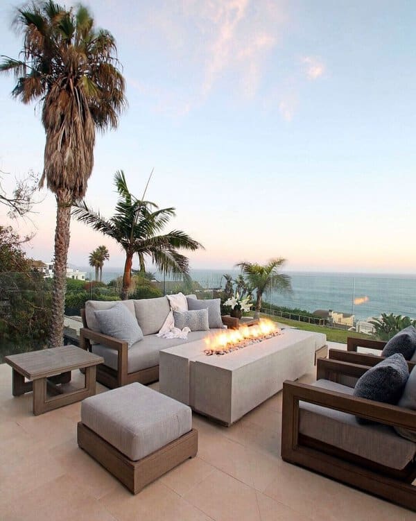 Outdoor patio with seating, fire pit, and ocean view under a clear sky with palm trees