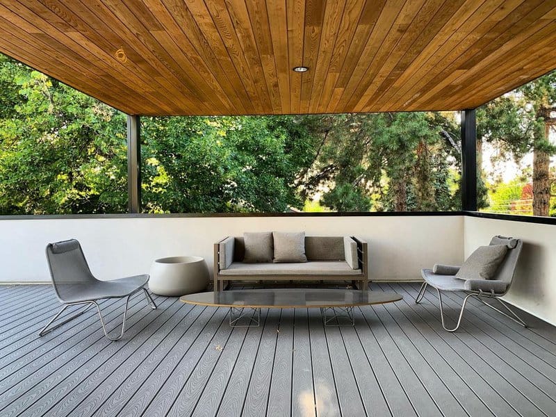 Modern patio with wooden ceiling, sofa, chairs, and trees in the background