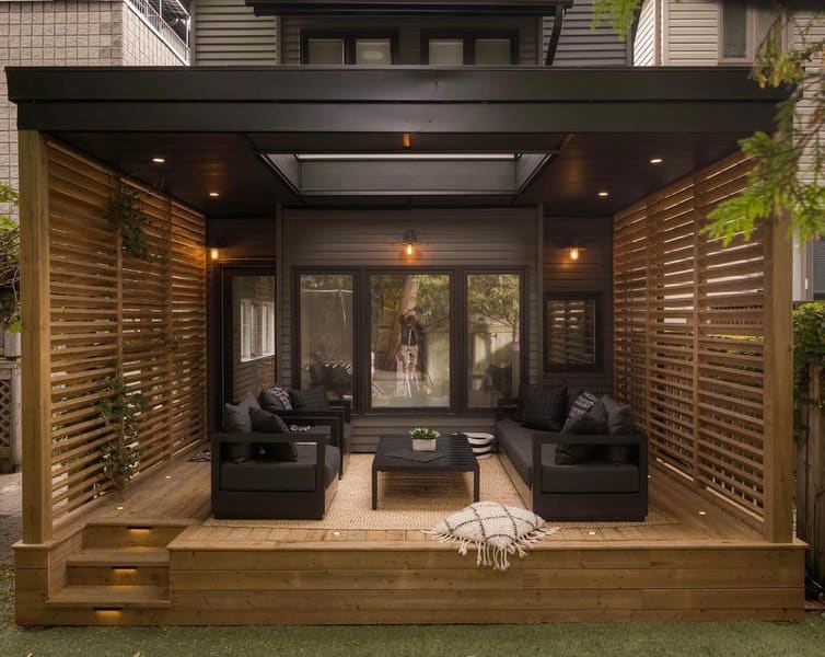 Modern patio with wooden slats, a glass roof, and black couches facing a central table