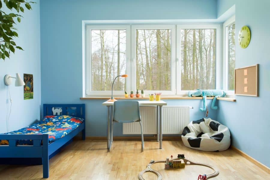 Pastel blue kids bedroom with single bed, study desk, and large window.