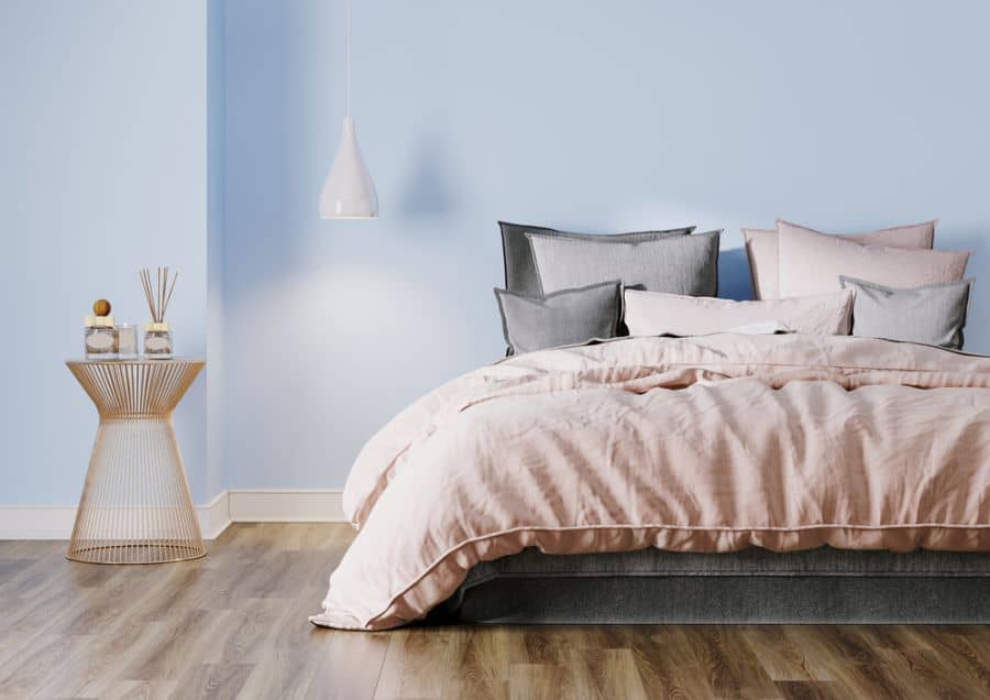 Pastel blue bedroom with laminate wood flooring, blush bedding, and pendant light.