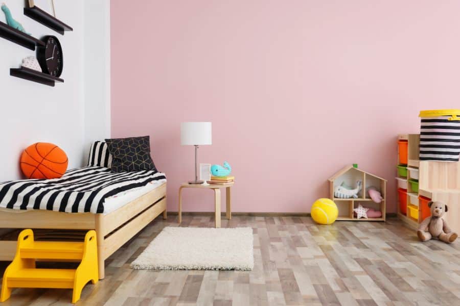 Pastel pink kids' bedroom with toy storage, dollhouse, and striped bedding.