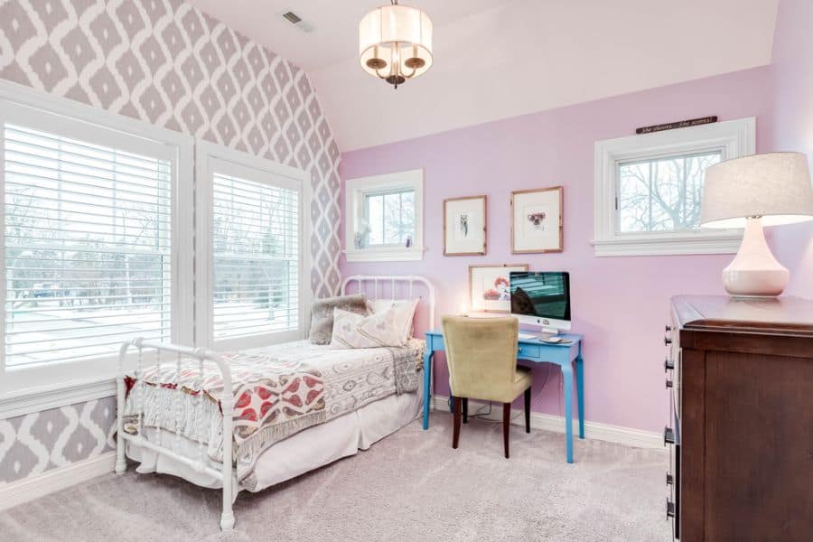 Pastel pink bedroom with single bed, blue desk, and patterned accent wall.