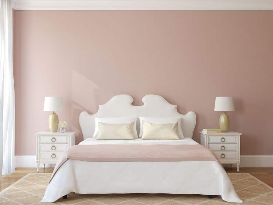 Pastel pink bedroom with white bed, matching nightstands, and table lamps.