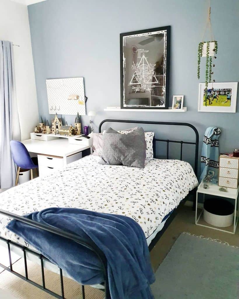 Blue boys bedroom with black metal bed, white desk, and framed wall art.