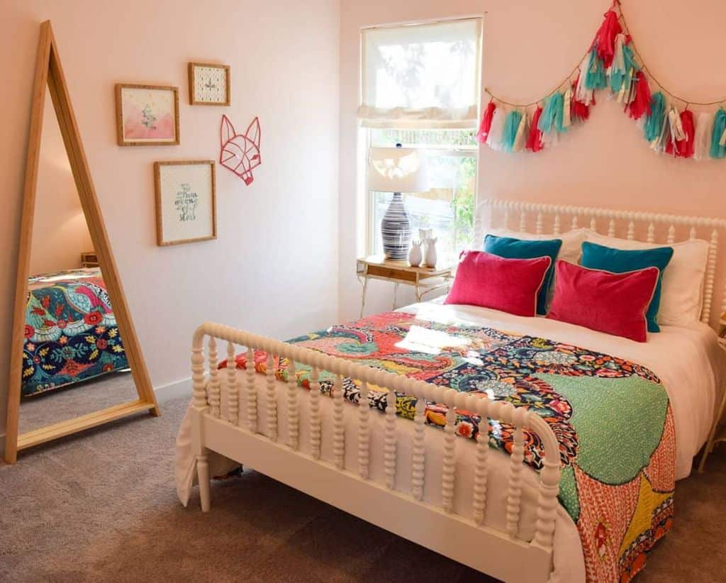 Kids bedroom with colorful bedding, tassel garland, framed wall art, and standing mirror.