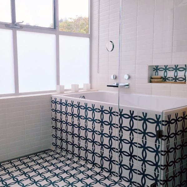 Bathroom with blue and white patterned tile bathtub surround, niche, and frosted windows.