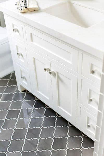 White bathroom vanity with silver knobs, over a grey patterned tile floor