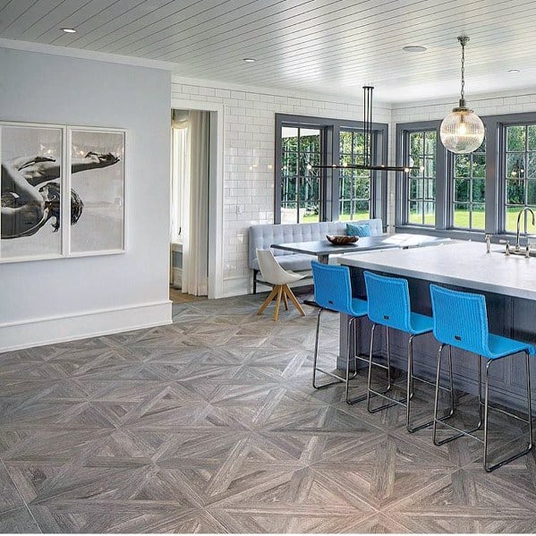 Modern kitchen with gray herringbone hardwood flooring, blue bar stools, and large windows offering a garden view