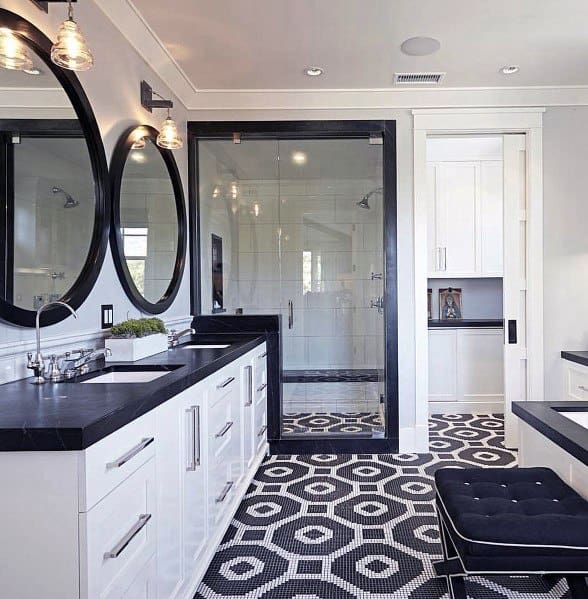 Black and white bathroom with hexagonal mosaic tile floor, round mirrors, and glass shower.