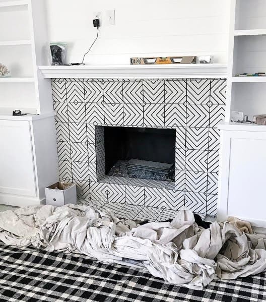 A chic fireplace design featuring intricate black-and-white patterned tiles, framed by built-in white shelving for a modern, bold aesthetic.