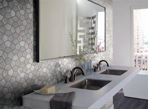 Geometric grey tile backsplash with dual sinks and modern bronze faucets.