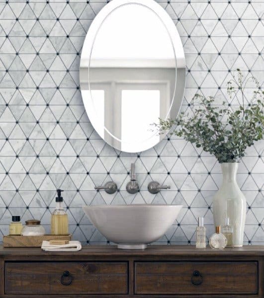 Bathroom with geometric tile backsplash, oval mirror, and wooden vanity.