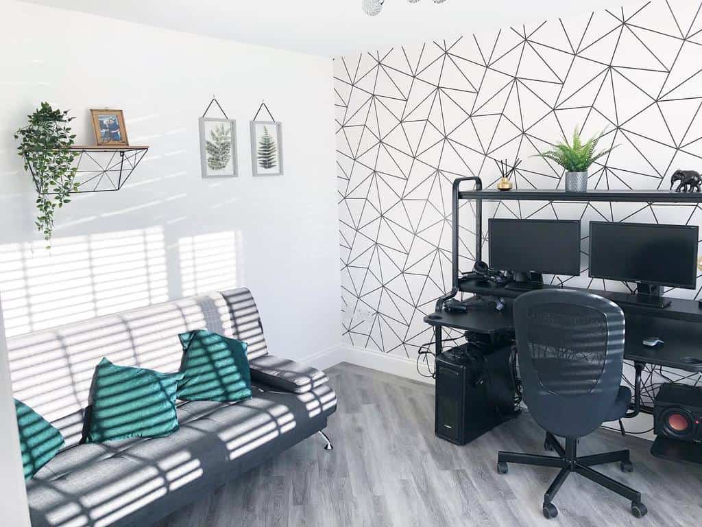 Modern home office with geometric wallpaper, black desk, dual monitors, and gray couch.