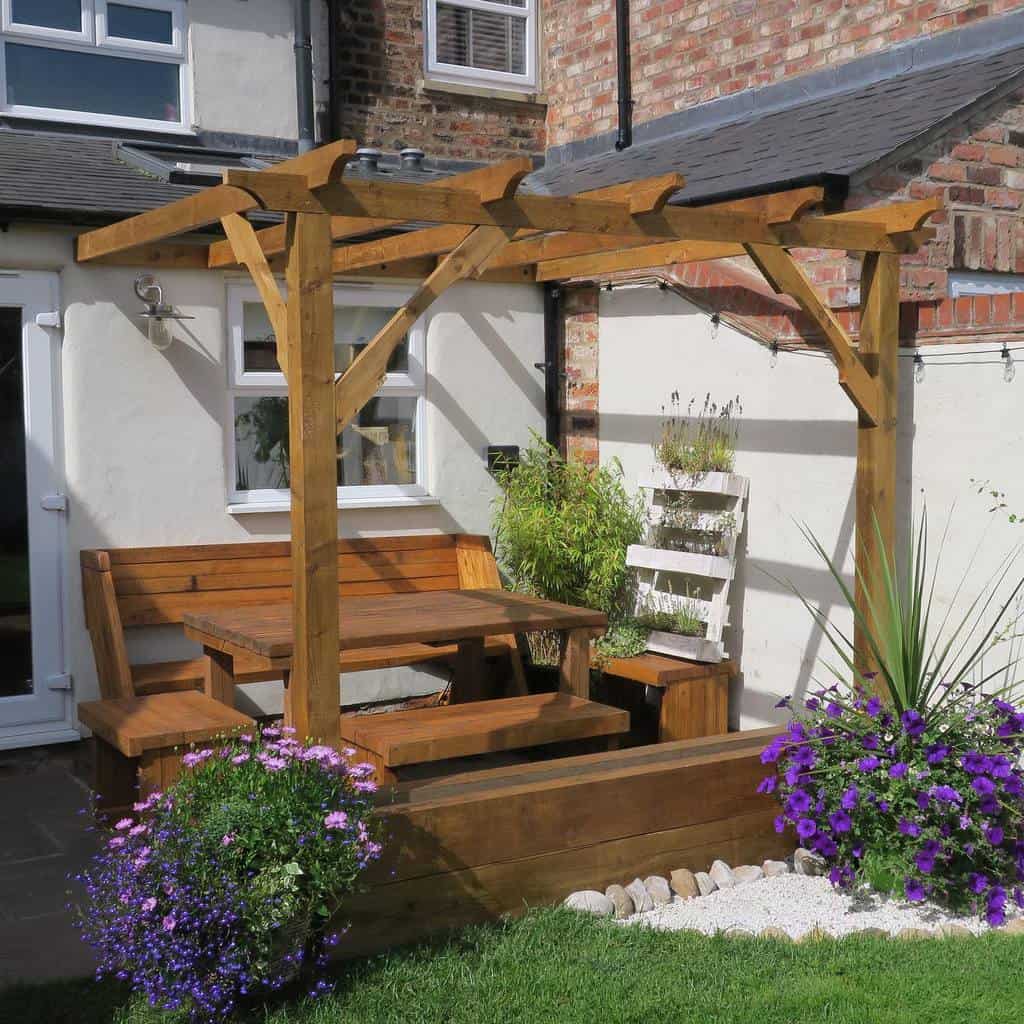 small backyard patio wood pergola wood table and chairs plants 