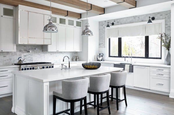 Elegant kitchen with large polished pendant lights hanging above a white island, complemented by soft gray stools and modern design elements