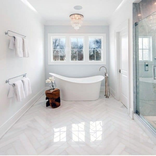 Bright bathroom with polished white herringbone floor tiles and a freestanding bathtub.