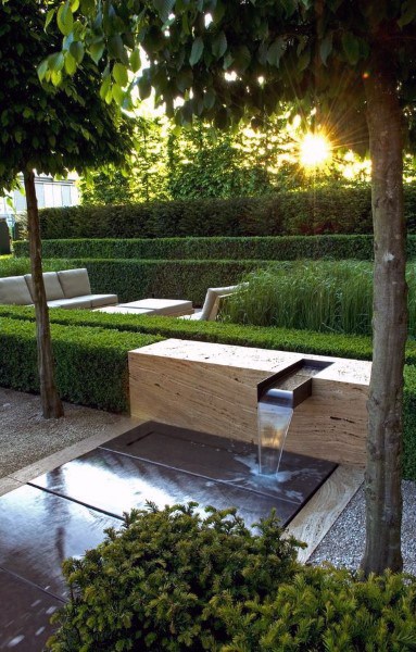 Minimalist waterfall feature with a sleek wooden design, surrounded by hedges and outdoor seating.