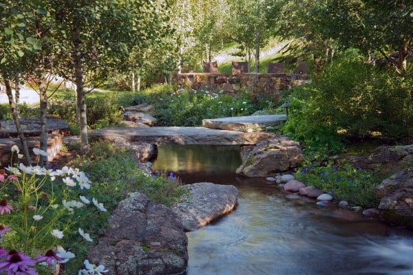 Tranquil stone-lined pond with flowers, trees, and natural stone bridges in a lush garden setting.