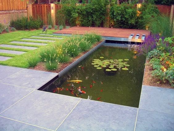 Rectangular pond with koi fish, water lilies, and a small waterfall, surrounded by sleek stone tiles and a wooden deck.