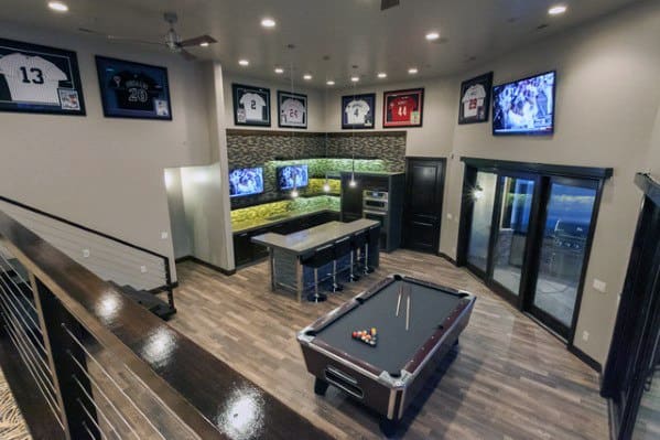 Modern mancave with pool table, sleek bar, framed jerseys, wood flooring, and large glass doors.