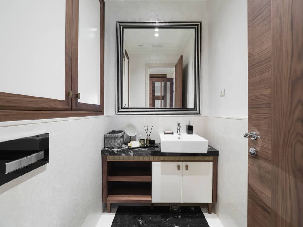 Modern bathroom with brown wood cabinetry, black marble countertop, and square vessel sink.