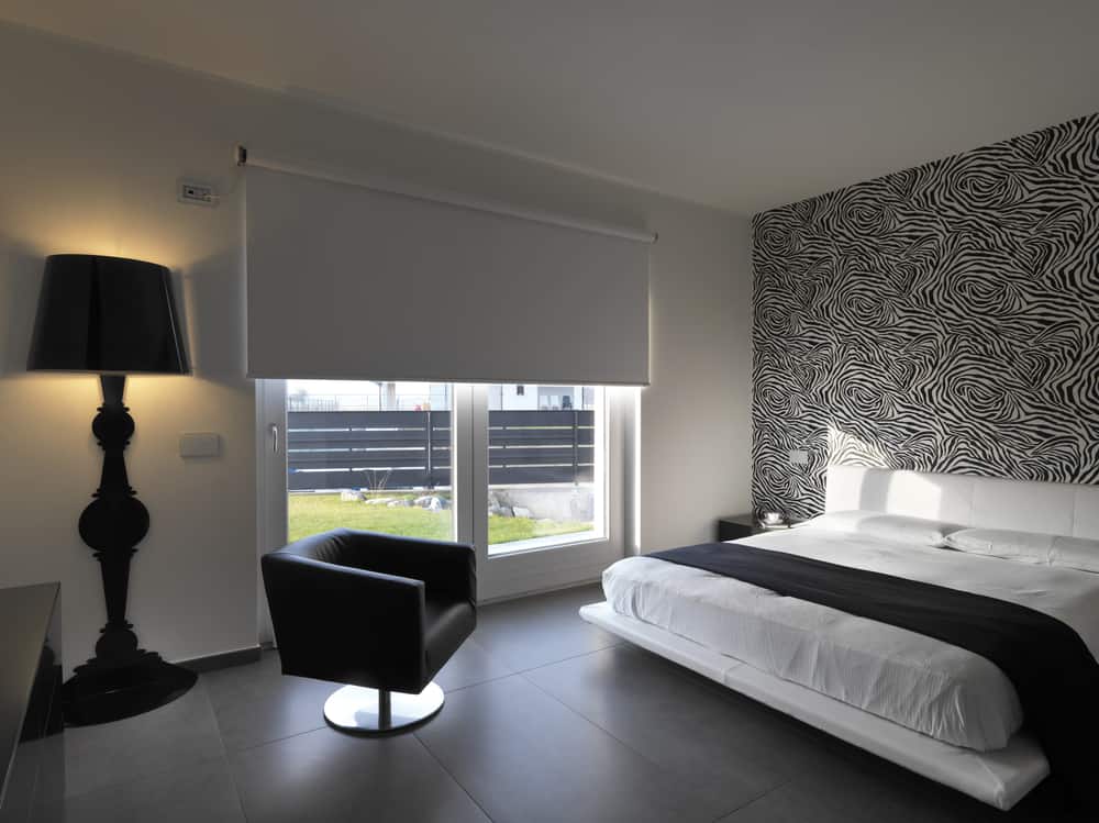 Modern bedroom with zebra-print wallpaper, white bed, tile flooring, and black accent furniture.