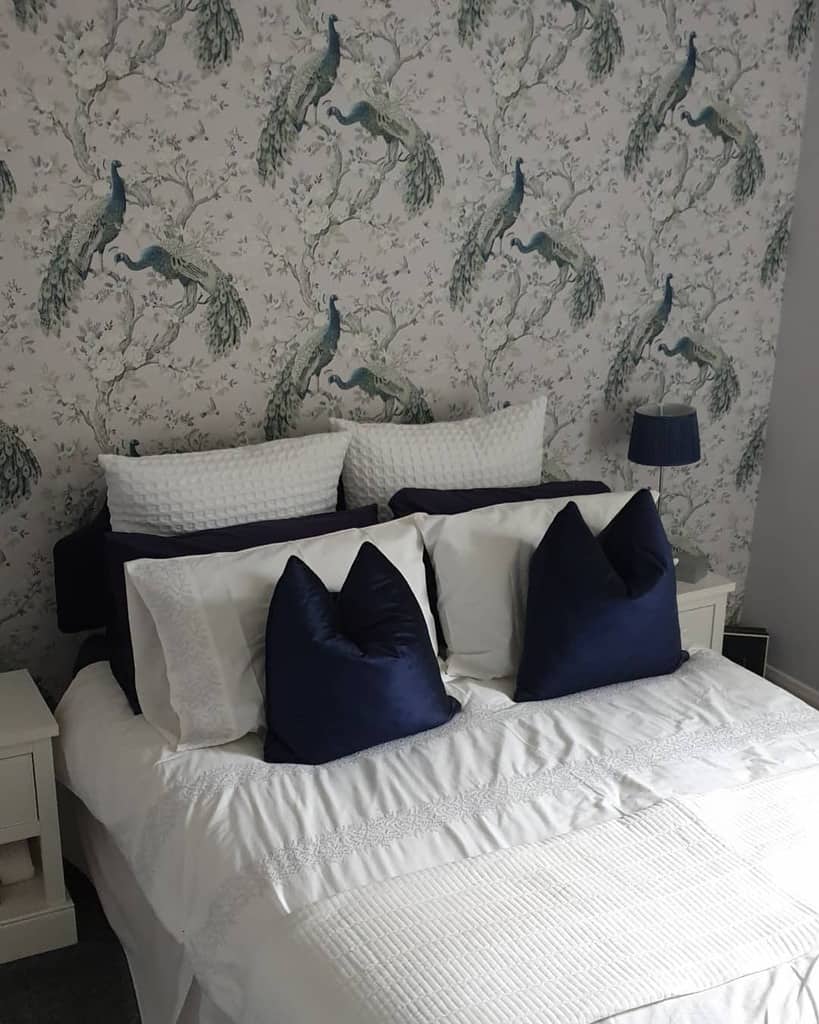 Bedroom with peacock-patterned wallpaper, white bedding, and navy accent pillows.