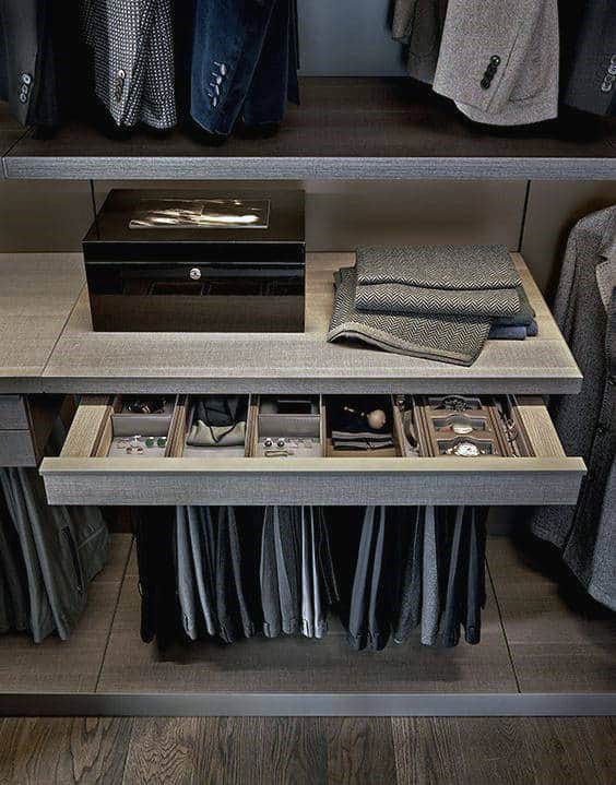 Open drawer with ties and accessories in a modern closet, suits and shirts hanging above and below