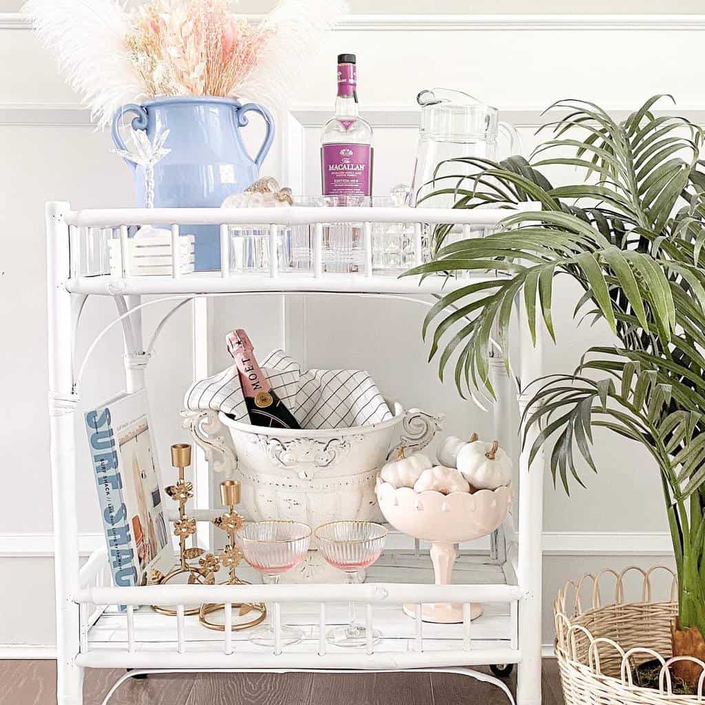 White wicker bar cart with pink champagne, candles, mini pumpkins, and floral decor.