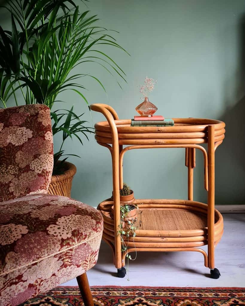 Rattan bar cart with books, vase, and plants next to a vintage floral armchair.