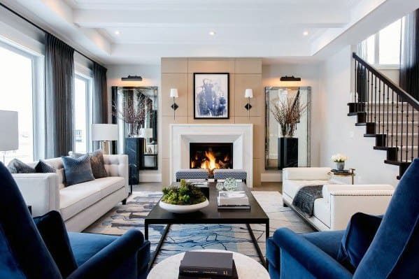 Modern living room with fireplace, white couches, blue chairs, and a large rug, decorated with mirrors and art