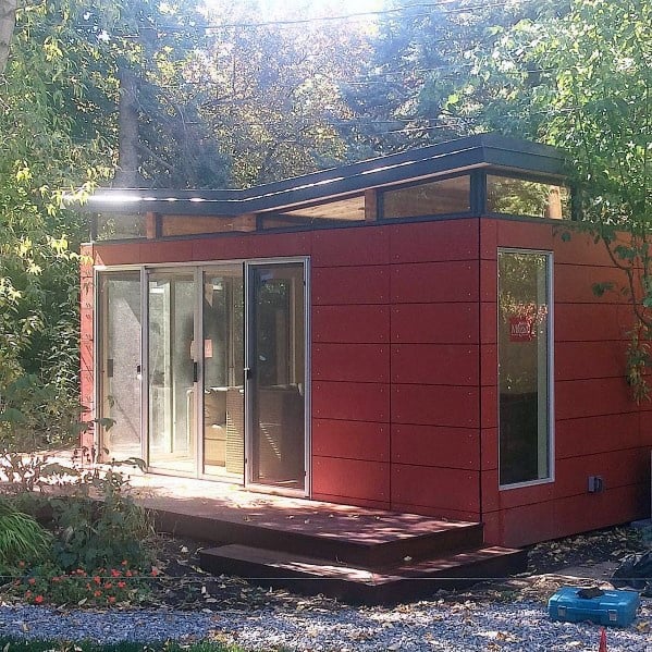 Modern red aluminum shed with sliding glass doors and raised wooden deck in a garden.