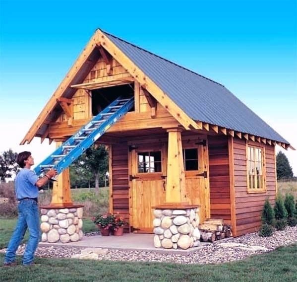 Rustic wooden shed with a metal roof, stone pillars, and canopy, featuring a loft and ladder.