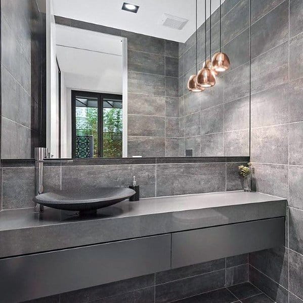 Modern bathroom with dark gray tiles, a black sink, and pendant lights above the mirror