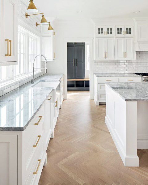 Elegant kitchen with herringbone wood flooring, white cabinets, marble countertops, and gold hardware