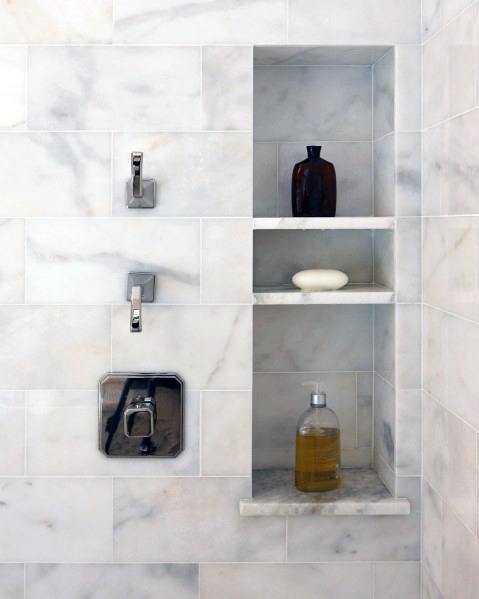 Marble shower with built-in shelves holding soap and bottles.