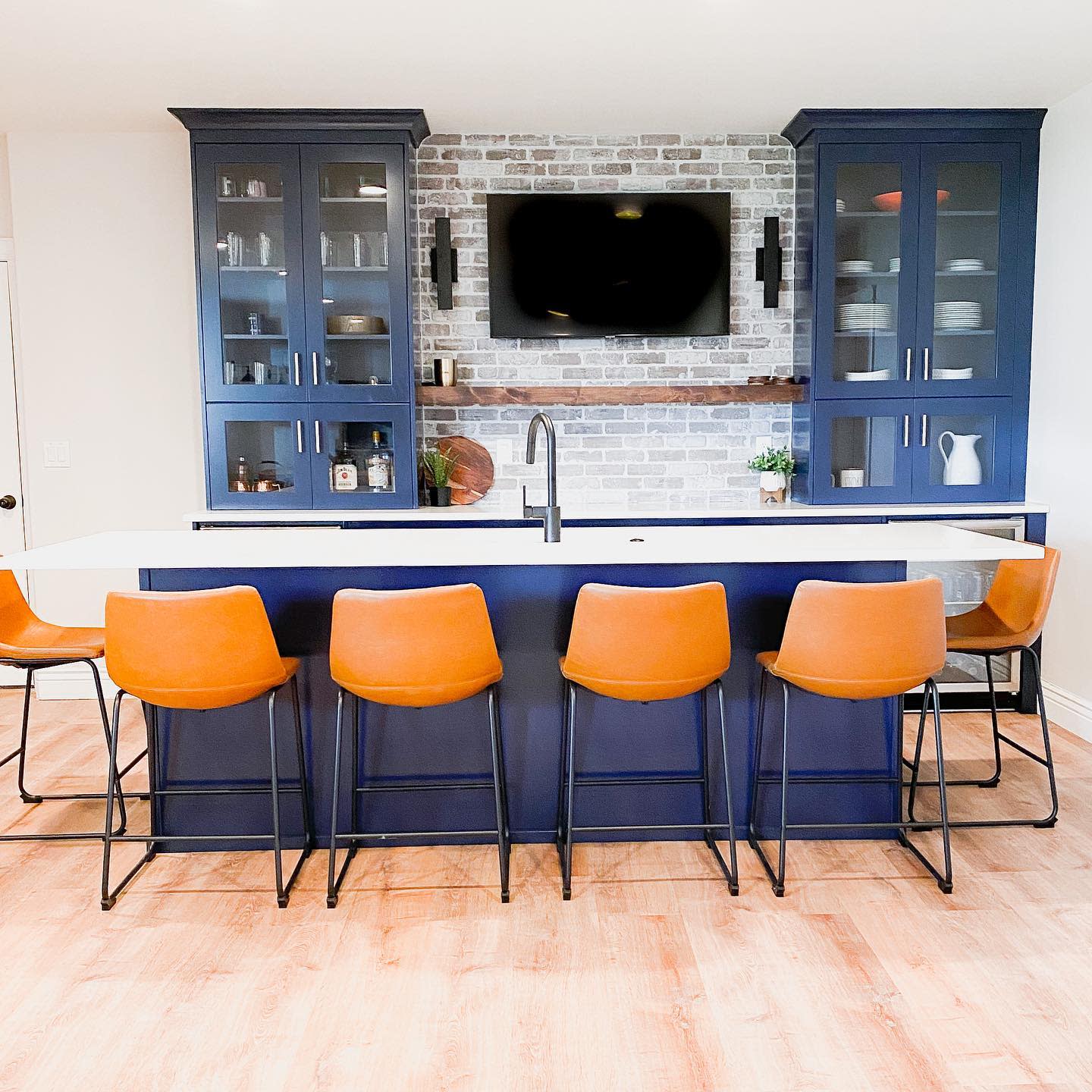 Large kitchen with blue cabinets, brick backsplash, and orange bar stools.