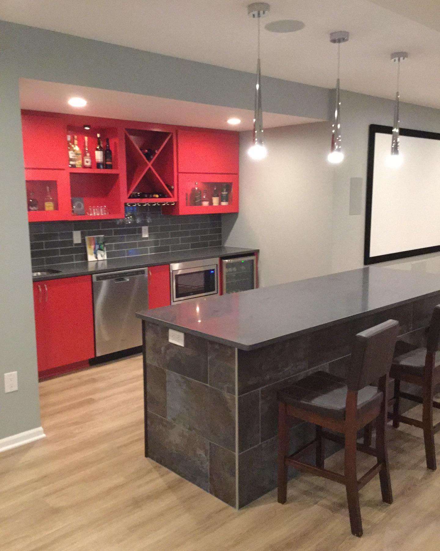 Basement kitchen with red cabinets, large gray island, and pendant lighting.